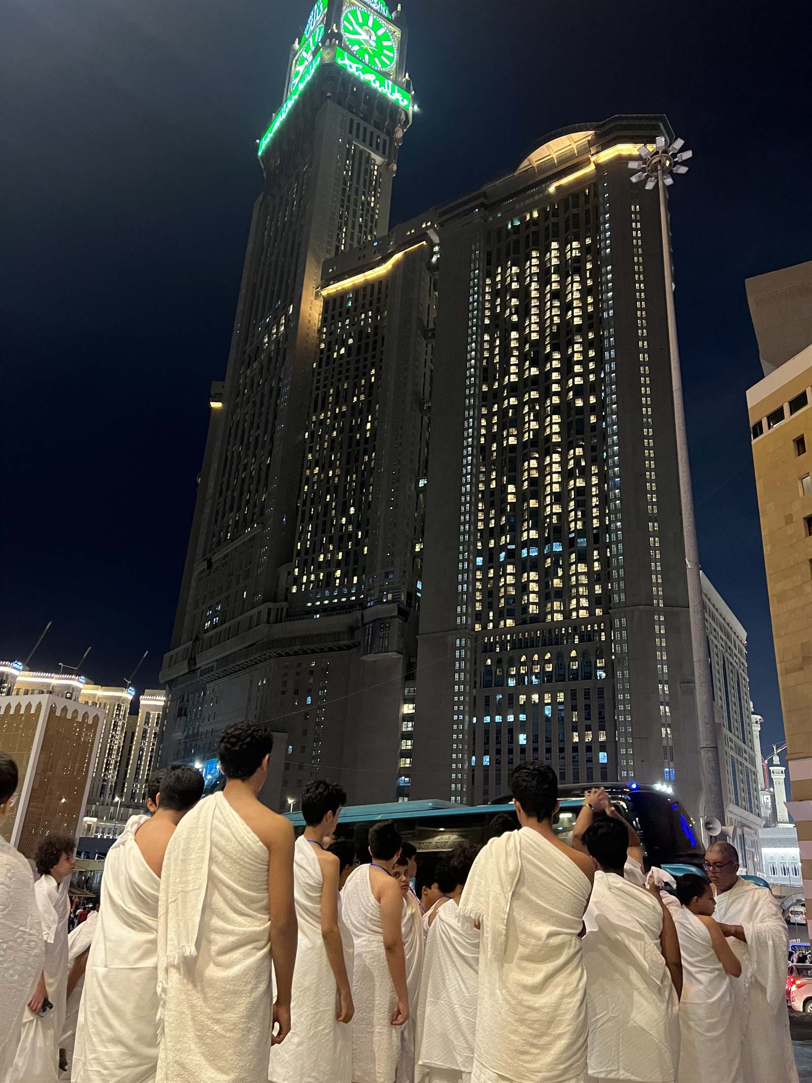 مجموعة بالإحرام تتجه نحو الحرم وبرج الساعة ليلًا